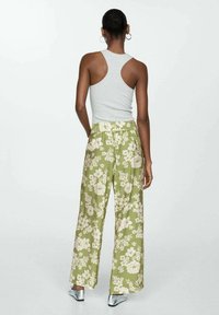 Lichtgrijs mouwloos tanktopje gecombineerd met wijde groene bloemenbroek met crèmekleurige bloemen en een textuurstof.