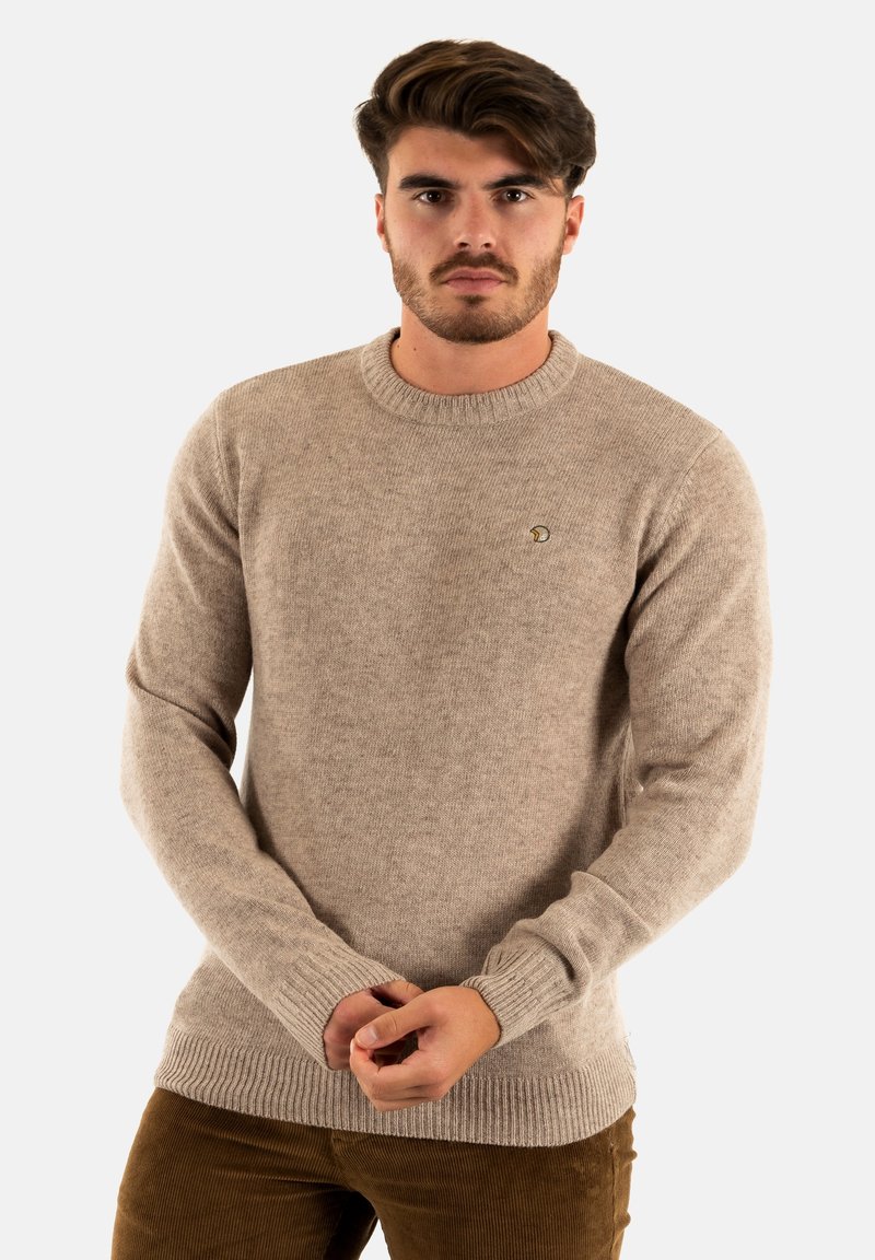 Pull en tricot beige avec un col ras du cou et des poignets côtelés. Présente un petit logo brodé sur la poitrine. Texture douce semblable à de la laine.