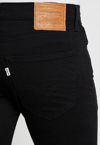 Vaqueros de denim negro con una etiqueta de cuero en la parte trasera de la cinturilla. Presenta bolsillos traseros cosidos con un diseño curvado distintivo.