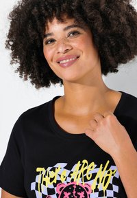 Sort bomulds T-shirt med korte ærmer, rund halsudskæring, med gul og lyserød grafisk tryk af en bjørn og tekst på et ternet mønster.