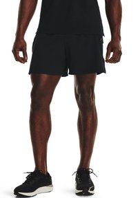 Shorts atléticos negros con un diseño ligero, textura suave y un ajuste relajado. Combinados con zapatillas de correr negras con suelas blancas.