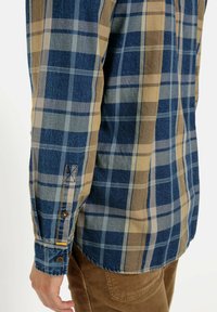 Geruite lange mouwen shirt in blauw en bruin tinten, met knoopmanchetten en contrasterende stoffen met variaties in textuur.