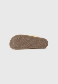 Sole of a shoe, featuring a textured brown rubber surface with circular and geometric grip patterns and a yellow upper edge.