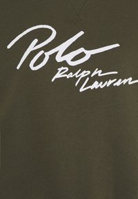 Tissu vert olive avec un grand texte en script blanc indiquant « Polo Ralph Lauren » imprimé dessus.