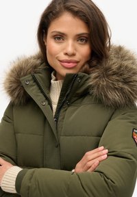 Olijfgroene pufferjack met een gefransde capuchon van bont, gequilt textuur, ritsluiting en ribgebreide manchetten voor extra warmte.