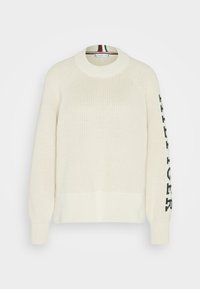 Maglione a maglia color crema con collo e polsini a costine, caratterizzato da testo logo nero lungo la manica sinistra. Tessuto strutturato e vestibilità rilassata.