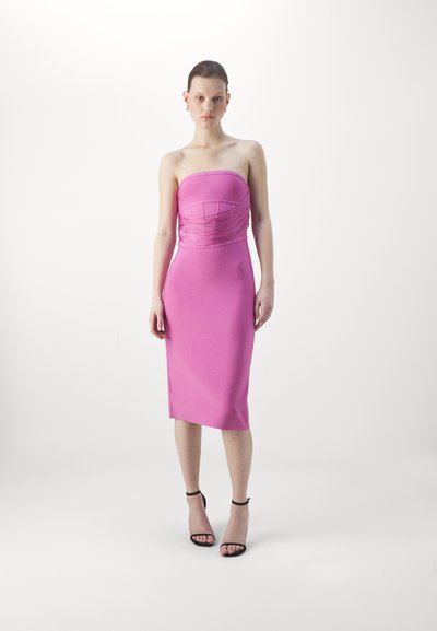Strapless pink bodycon dress with ruched detailing at the bodice, smooth texture, knee-length, paired with black ankle strap heels.
