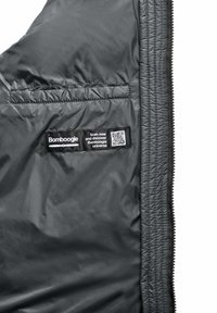 Zwarte, gewatteerde binnenkant van het jack met een zijzak. Etiket bevat een QR-code en de tekst "Bombogie" op een textuurstof patch.