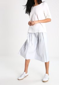 White blouse with short puff sleeves, paired with a light blue pleated midi skirt and white sneakers with tan soles.