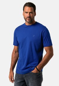 T-shirt s krátkým rukávem a kulatým výstřihem v živé modré barvě z bavlny, s jemným detailem loga na hrudi, spárovaný s tmavými džíny.