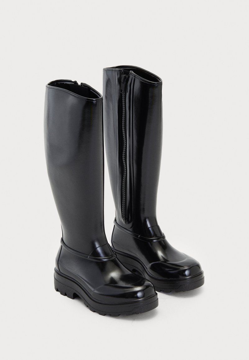 Knee-high mustad mustadöödiga mustad kummisaapad läikiva viimistlusega, külgsulgemisega ja tekstuuriga tallaga, et tagada haarduvus. Ümar varvas.