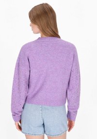 Lawendowy sweter o fakturowym wykończeniu z prążkowanym dołem, balonowymi rękawami i wzorzystymi otworami na rękawach. Połączony z jasnymi dżinsowymi szortami.