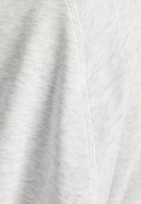 Ljust grått tyg med en slät, något strukturerad yta och subtil mönstring. Har synlig sömnad längs kanten.