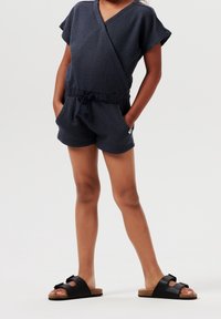 Mono de textura azul marino con diseño cruzado, mangas cortas y cintura con tirante elástico, combinado con sandalias negras con detalle de lazo.