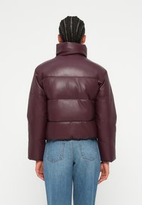 Veste courte en duvet bourgogne en matériau brillant, avec un rembourrage horizontal et un col montant, associée à un jeans en denim taille haute.