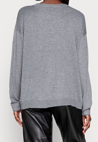 Pull gris surdimensionné avec un col arrondi, des manches longues et des poignets côtelés. Le tissu semble doux avec une texture lisse.