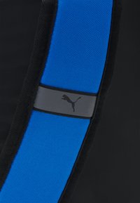 Črn športni material s širokim modrim teksturiranim trakom in sivim trakom, ki vsebuje črn logotip. Oblika je elegantna in sodobna.