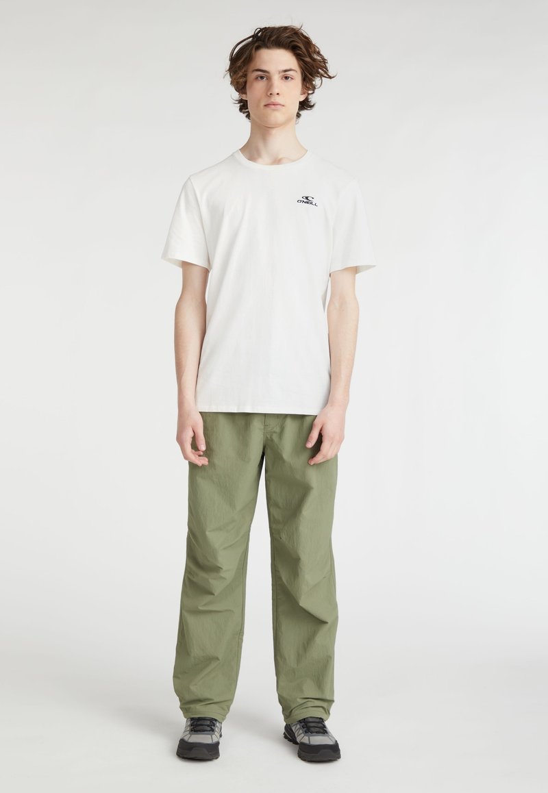 Witte katoenen T-shirt met een klein zwart logo, gecombineerd met loszittende olijfgroene broek. De outfit wordt afgemaakt met grijze sneakers.