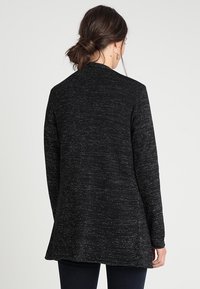 Maglione lungo a trama nera e argento con vestibilità rilassata, scollatura rotonda e maniche lunghe, che arriva a metà fianchi. Senza chiusure visibili.
