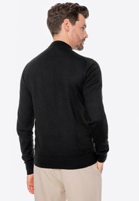 Schwarze, langärmlige Strickjacke mit geripptem Kragen und Bündchen, glatter Textur, taillierter Form und bandierter Säume. Ansicht von hinten.