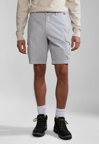 Pantalones cortos de carga grises claros con bolsillos laterales, un diseño de frente plano y un ajuste cómodo, combinados con botas de senderismo negras y calcetines blancos.
