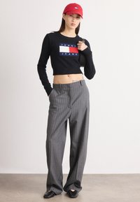 Černý zkrácený svetr s bílým a modrým logem "TOMMY JEANS", doplněný o šedé pruhované široké kalhoty a červenou čepici.