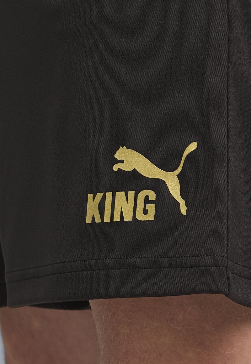 Sorte atletiske shorts lavet af blødt stof, med en guldsilhuet af en springende puma og ordet "KING" i fed skrift.