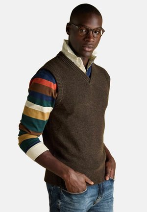 Braune gestrickte Weste mit V-Ausschnitt, die über einem langärmligen, mehrfarbig gestreiften Shirt getragen wird. Sie verfügt über gerippte Kanten und eine strukturierte Oberfläche.