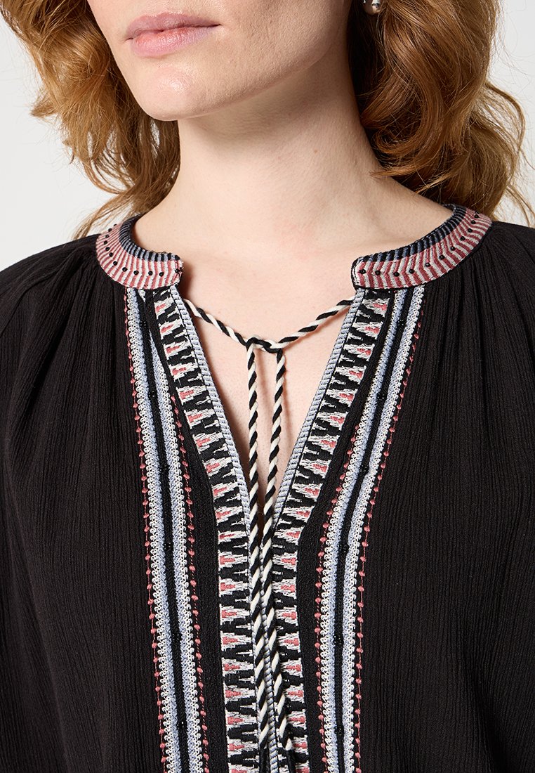 Schwarze Bluse mit dekorativem Ausschnitt, geflochtenen Bändchen, aufwendiger mehrfarbiger Stickerei und strukturierter Stoff.