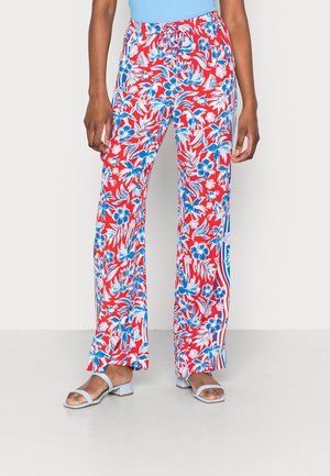 Person trägt weit geschnittene Hosen mit roten, blauen und weißen Blumenmustern, einem Kordelzug in der Taille und hellblauen Sandalen mit offenen Zehen und niedrigem Absatz.