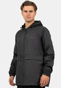 Zwarte lichtgewicht regenjas met een rits aan de voorkant, verstelbare capuchon en elastische manchetten; heeft twee voorkeepockets en een gladde textuur.