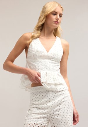 Haut sans manches blanc avec un décolleté en V, une taille peplum et un motif à œillets, associé à un pantalon assorti présentant un design découpé similaire.