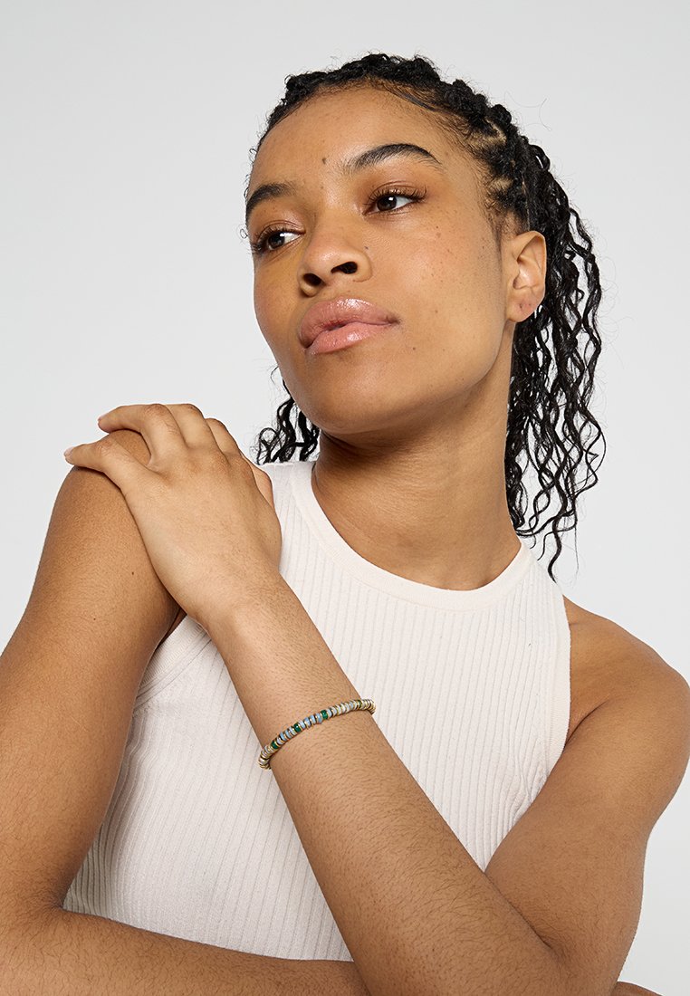 Perlenarmband mit verschiedenen farbigen Perlen und einem Akzent in Goldton, am Handgelenk getragen vor einem neutralen Hintergrund.