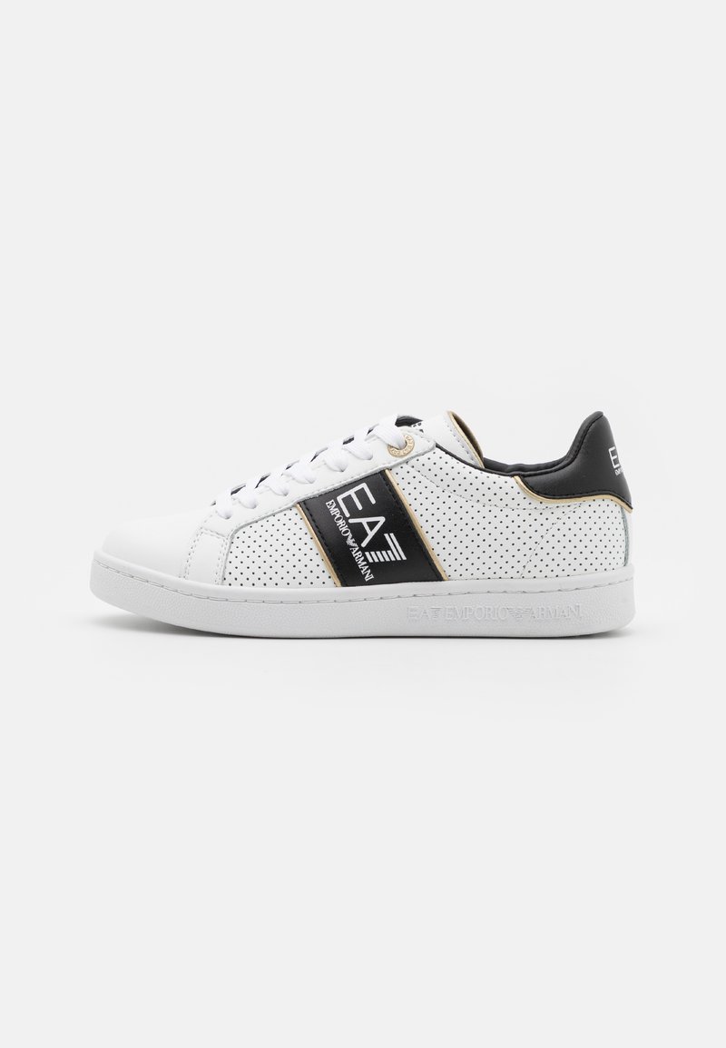 Weißer Sneaker aus perforiertem Leder mit schwarzen Akzenten und einem gebrandeten Riemen. Schnürverschluss und strukturierte Gummisohle.