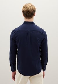 Camisa de manga larga azul marino con cuello abotonado, detalle de canesú en la espalda y dobladillo redondeado. Hecha de una tela texturizada.