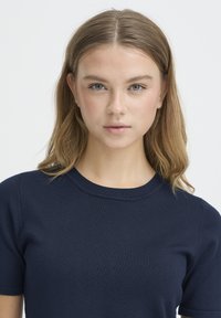 Haut court en maille bleu marine avec manches courtes, col rond et texture côtelée, présentant une silhouette ajustée et des détails minimalistes.