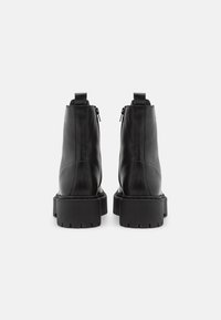 Botas de cuero negro hasta el tobillo con una suela de plataforma resistente, cremallera trasera y tira de agarre. Textura suave y diseño simple.