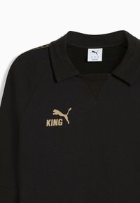 Polo de sport noir avec col, arborant un logo doré "KING" et un emblème Puma. Conçu pour un look athlétique décontracté.