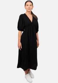 Abito nero al ginocchio in un tessuto texturizzato con maniche a sbuffo e scollatura a V. Abbinato a sneakers bianche per un look informale.