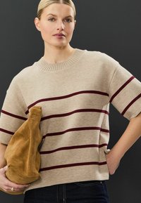 Beige strikket sweater med maroon horisontale striber, korte ærmer og en ribbet rund halsudskæring, parret med en brun ruskinds clutch taske.