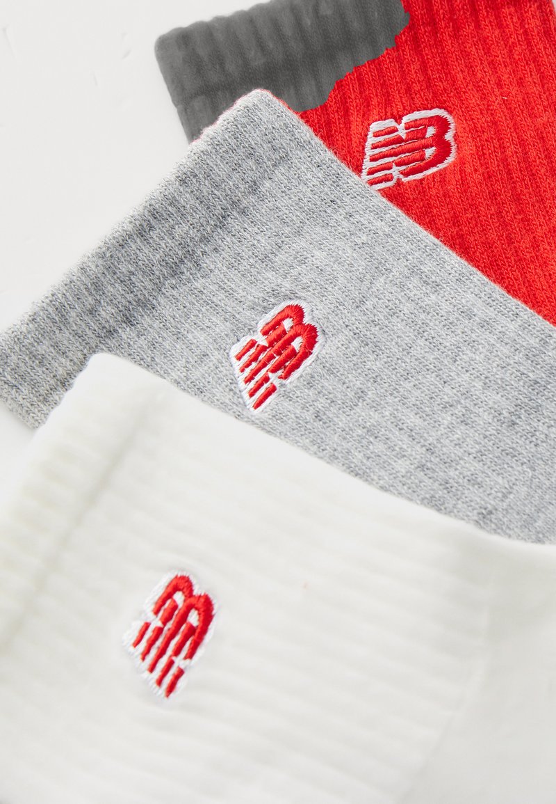 Tres pares de calcetines: blanco, gris y rojo. Cada uno presenta un logo con acentos rojos, punto texturizado y puños acanalados.