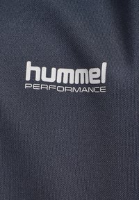 hummel Performance logo i hvid på mørkegrå tekstureret stofbaggrund