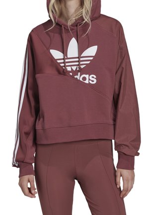 Femme portant un sweat à capuche adidas marron avec logo blanc et bandes sur les manches, associé à un legging marron assorti.