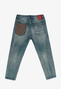 Džínové kalhoty světle modré barvy s vybledlým efektem. Mají dvě zadní kapsy: jedna hladká a druhá s aplikací v hounds-tooth vzoru a červenou etiketou.