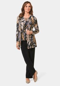 Langärmliges Top mit Blumenmuster in Schwarz-, Beige- und Blautönen, kombiniert mit schwarzen, weiten Hosen und beigen Absatzschuhen.