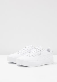 Weiße Sneakers mit einem glatten synthetischen Obermaterial, runder Zehenpartie und einer dicken Gummisohle. Zu den Merkmalen gehören flache Schnürsenkel und ein dezentes Logodetail.