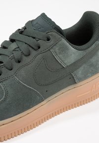 Baskets Nike en daim vert foncé avec lacets noirs et col rembourré, dotées d'une semelle en caoutchouc beige avec le logo "AIR".