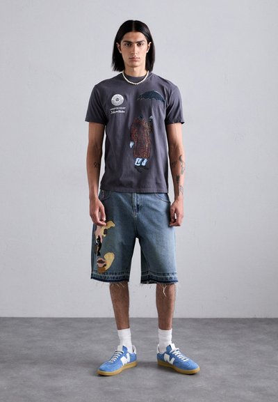 Gray graphic t-shirt featuring an umbrella and a figure design; paired with denim shorts displaying abstract patterns and frayed hems. Blue sneakers.