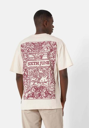 Beige cotton t-shirt featuring a large maroon graphic design on the back, with intricate details and text reading "SIXTH JUNE." Short sleeves.