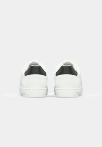 Baskets blanches avec une finition en cuir lisse, présentant un accent noir au niveau du talon et une semelle en caoutchouc blanche. Design minimaliste, lignes épurées.